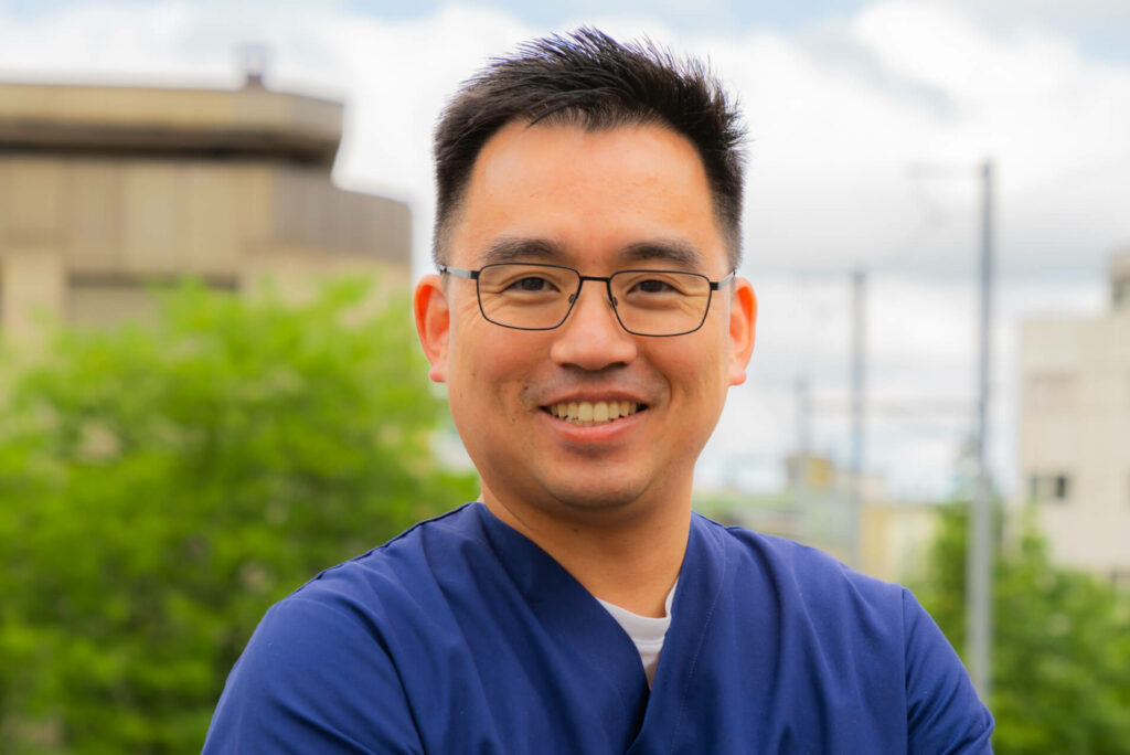 Freundlicher Zahnarzt Dr.Jeong-Woo Yoo von Smilezone Zug mit Brille und blauem Praxis-Outfit